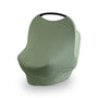 The mushie Multi-Use Cover in green is shown fitted over a baby car seat, covering the seat and all but the top of its black handle, against a plain white background.