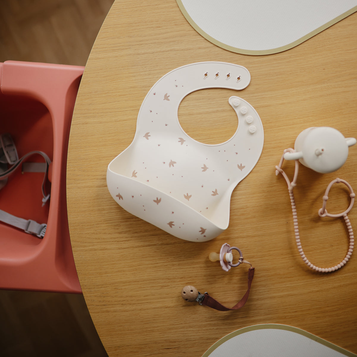 Mushie Silicone Baby Bib with pacifier and teether set displayed on a wooden table.