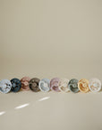 Nine FRIGG Moon Natural Rubber Pacifier 2-Packs lined up on a neutral background.