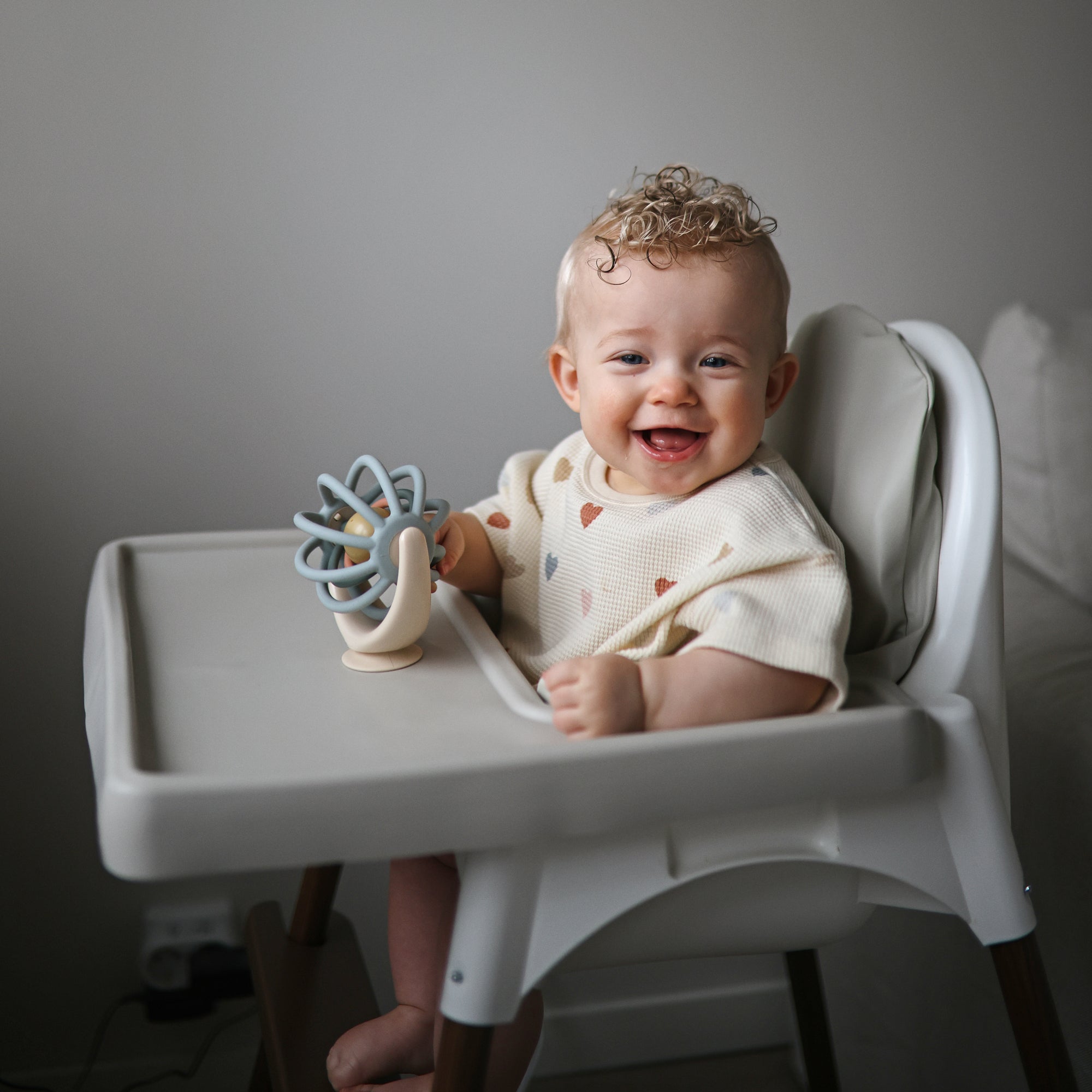 Baby sitting in a high chair with a suction spinner ball toy, smiling.