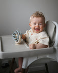 Baby sitting in a high chair with a suction spinner ball toy, smiling.