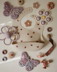Mushie Silicone Sensory Toy and bibs in pink and purple on a light background.