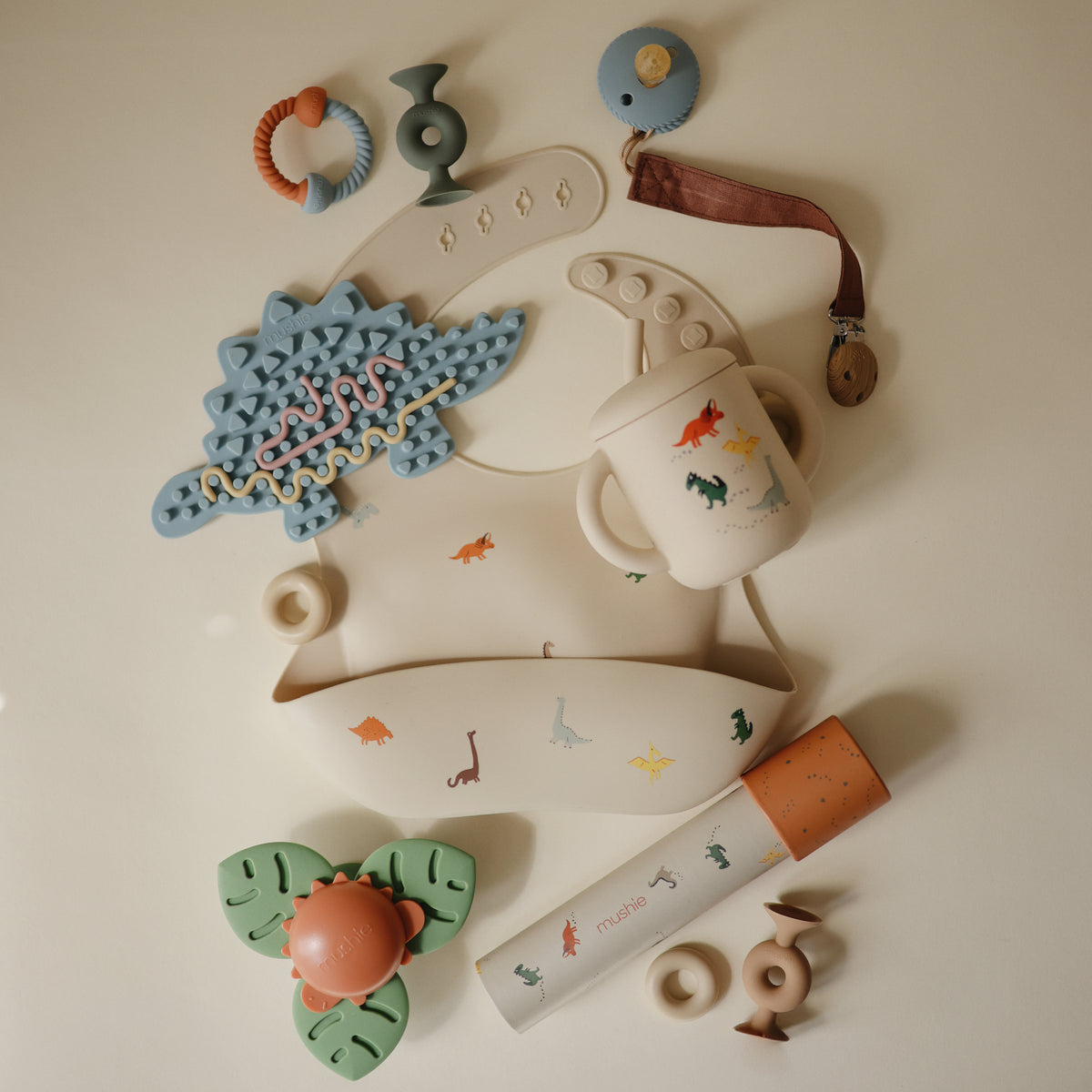 Mushie Silicone Sensory Toy: dinosaur-themed beige baby teething and feeding accessory.