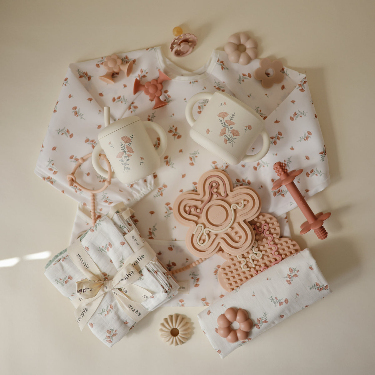 Mushie Silicone Sensory Toy and baby items arranged on a cream background.