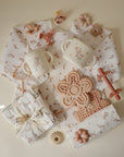 Mushie Silicone Sensory Toy and baby items arranged on a cream background.