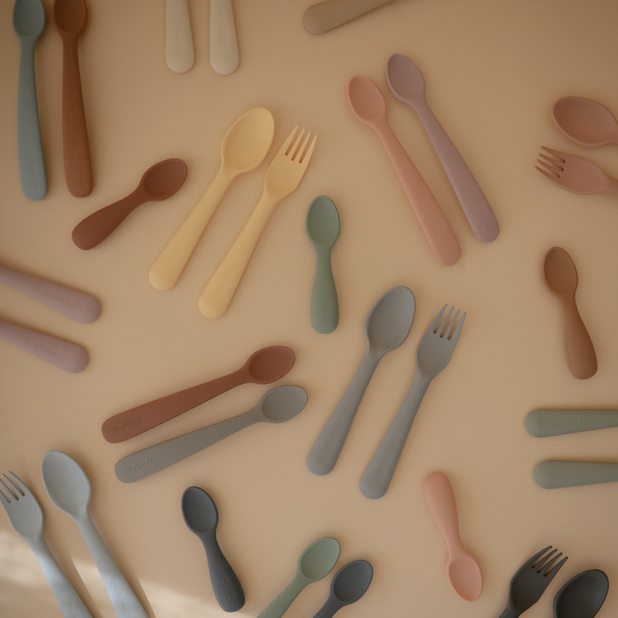 Mushie Dinnerware Fork and Spoon Set, dishwasher-safe, arranged on a beige surface flat lay.