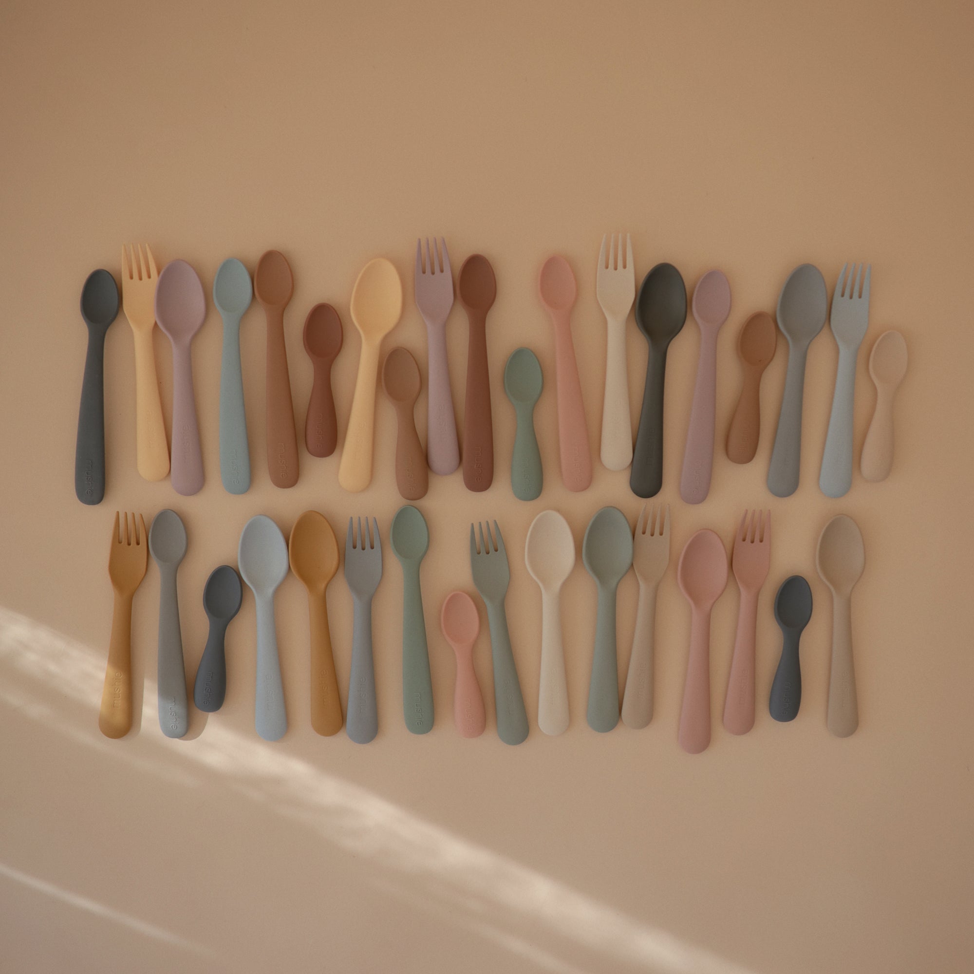 Rows of colorful mushie Dinnerware Fork and Spoon Sets on a beige background.