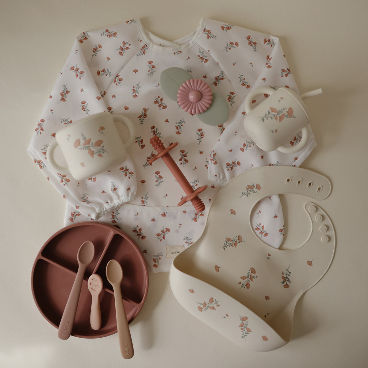 Mushie Long Sleeve Bib, silicone bib, divided plate, two cups, two spoons, and a teething toy.