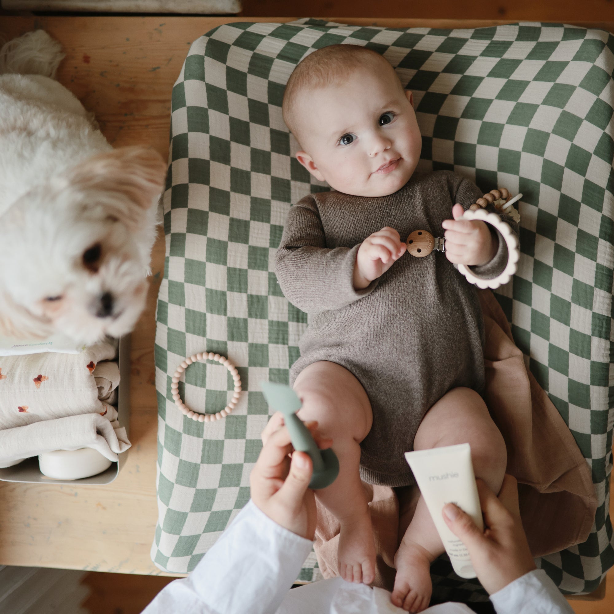 Baby lies on a green-checkered mat; use mushie Baby Cream to soothe dry skin.