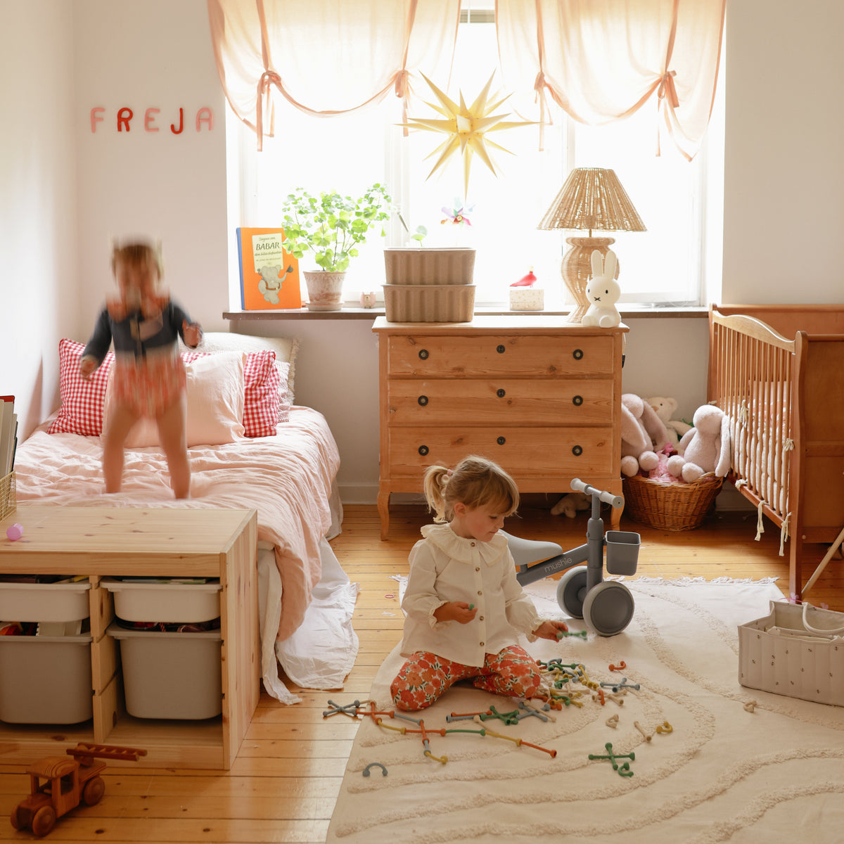 Two kids play in a bright room; a mushie Mini Toddler Bike sits among their scattered toys.