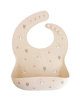 Mushie Silicone Baby Bib—beige with colorful cup and challah design, adjustable neck strap.