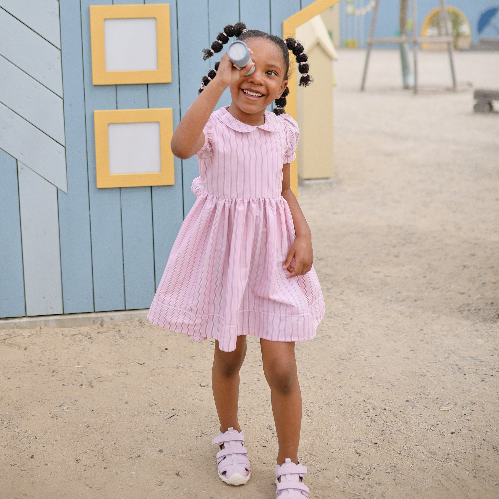 A smiling girl in pink enjoys outdoor imaginative play with a mushie Kaleidoscope.