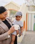 Smiling woman holds baby with FRIGG Moon Natural Rubber Pacifier 2-Pack at playground.