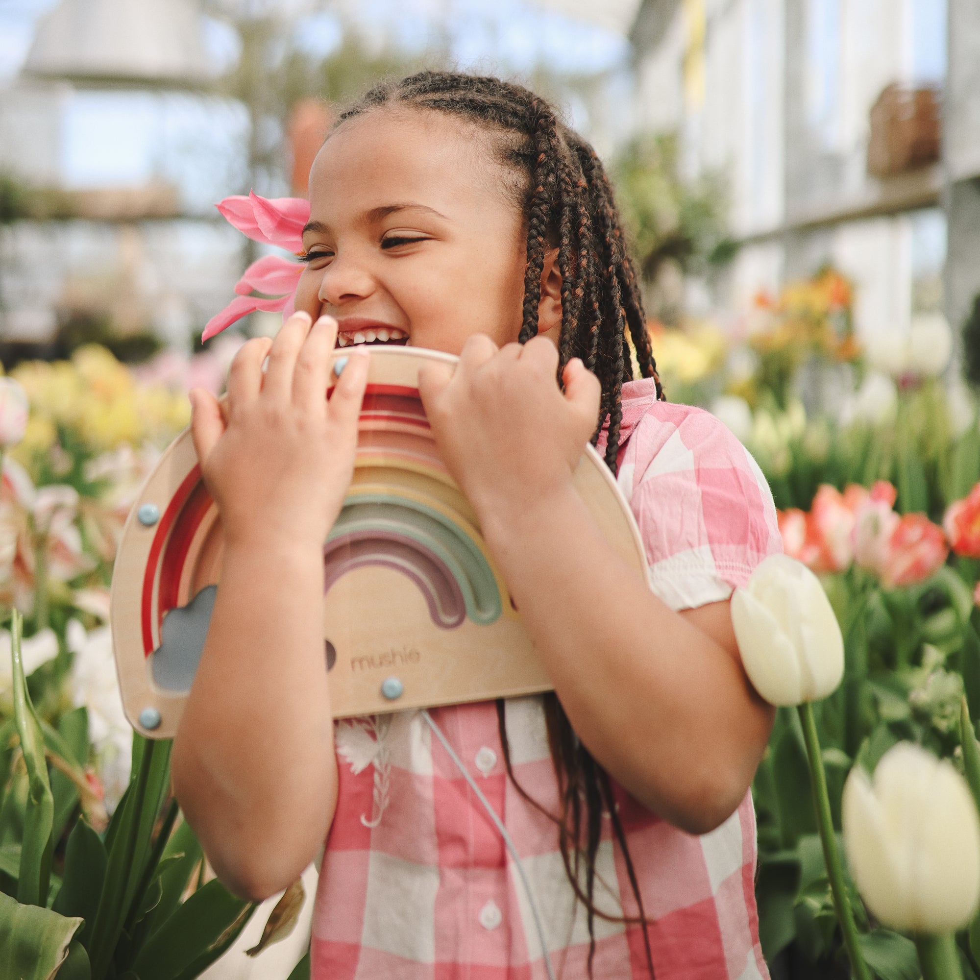 Smiling girl plays outdoors with mushie's Wooden Magnetic Rainbow Maze for screen-free fun.