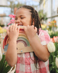 Smiling girl plays outdoors with mushie's Wooden Magnetic Rainbow Maze for screen-free fun.
