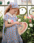 Young girl in a blue floral dress holds the mushie Wooden Magnetic Rainbow Maze by tulips.