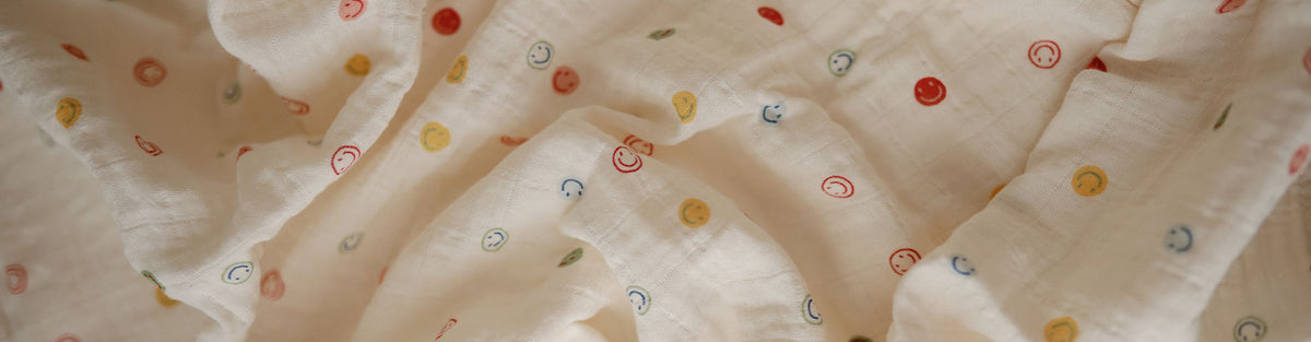 Close-up of a soft, off-white fabric with a delicate pattern of small, scattered smile outlines in red, yellow, blue, and green.