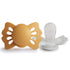 The FRIGG Lucky Symmetrical Silicone Pacifier 2-Pack (0-6 Months) by FRIGG features two pacifiers: one with a mustard yellow butterfly-shaped shield and one showing its medical grade silicone nipple and white base for baby’s comfort and safety.