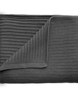 The mushie Knitted Ribbed Baby Blanket in dark gray is neatly folded with a corner turned over, showing its textured ribbed design on both sides against a white background.