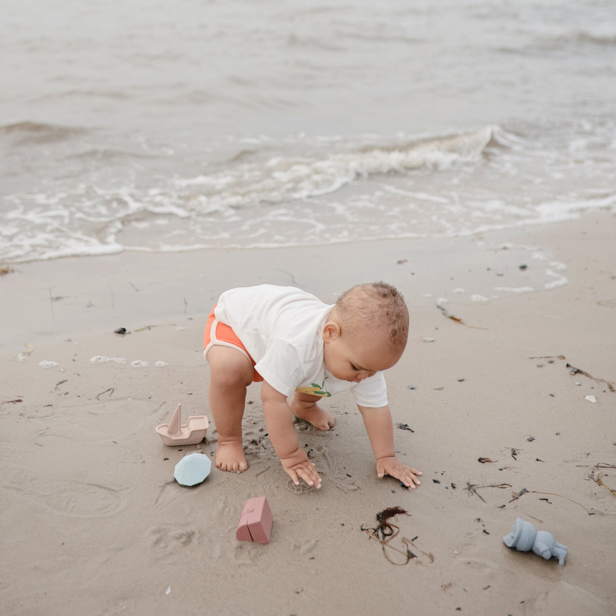 Lifestyle image of a baby playing on a sandy beach with the mushie Pirate Bath Play Set. 