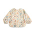 The mushie Long Sleeve Bib in Space features a colorful, pastel space-themed pattern, elastic cuffs, water-resistant material, a wipe-clean surface, and a handy bottom pocket—perfect for kids.