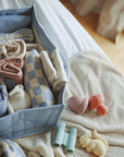 Lifestyle image of folded clothes stored in a Tradewinds Diaper Caddy next to baby toys on a blanket. 