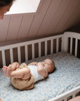 A baby on a mushie Extra Soft Muslin Crib Sheet looks up at an adult from the crib.