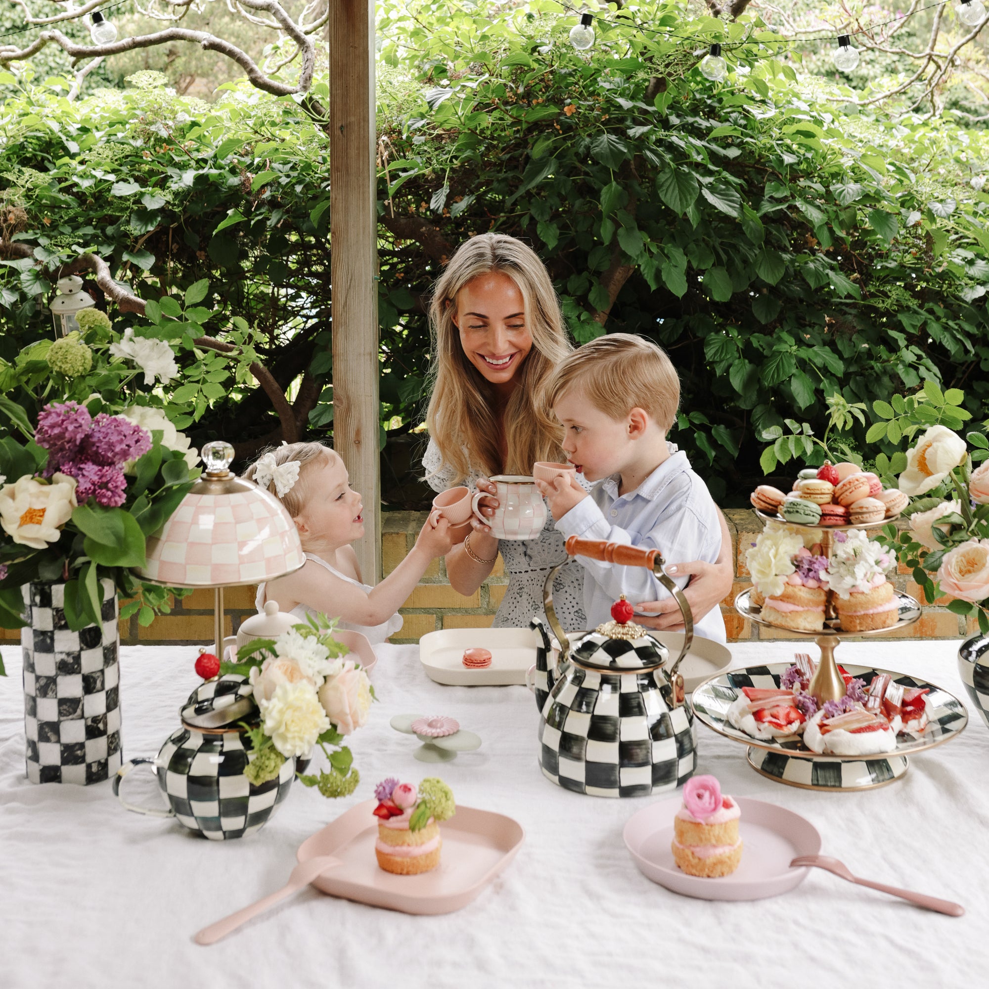 A woman and two kids use mushie's Dinnerware Fork and Spoon Set at a lovely outdoor tea table.