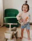 Smiling toddler plays with mushie's Elastic Shape Sorter, building fine motor skills.