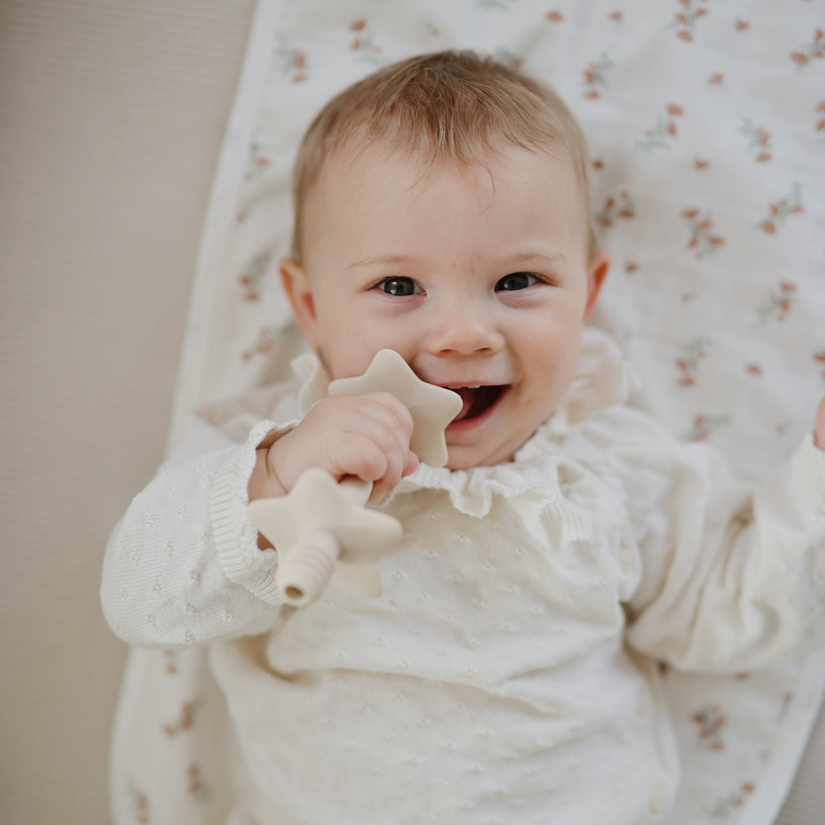 A happy baby on a Mushie Changing Pad Liner, chewing on a star-shaped teether.