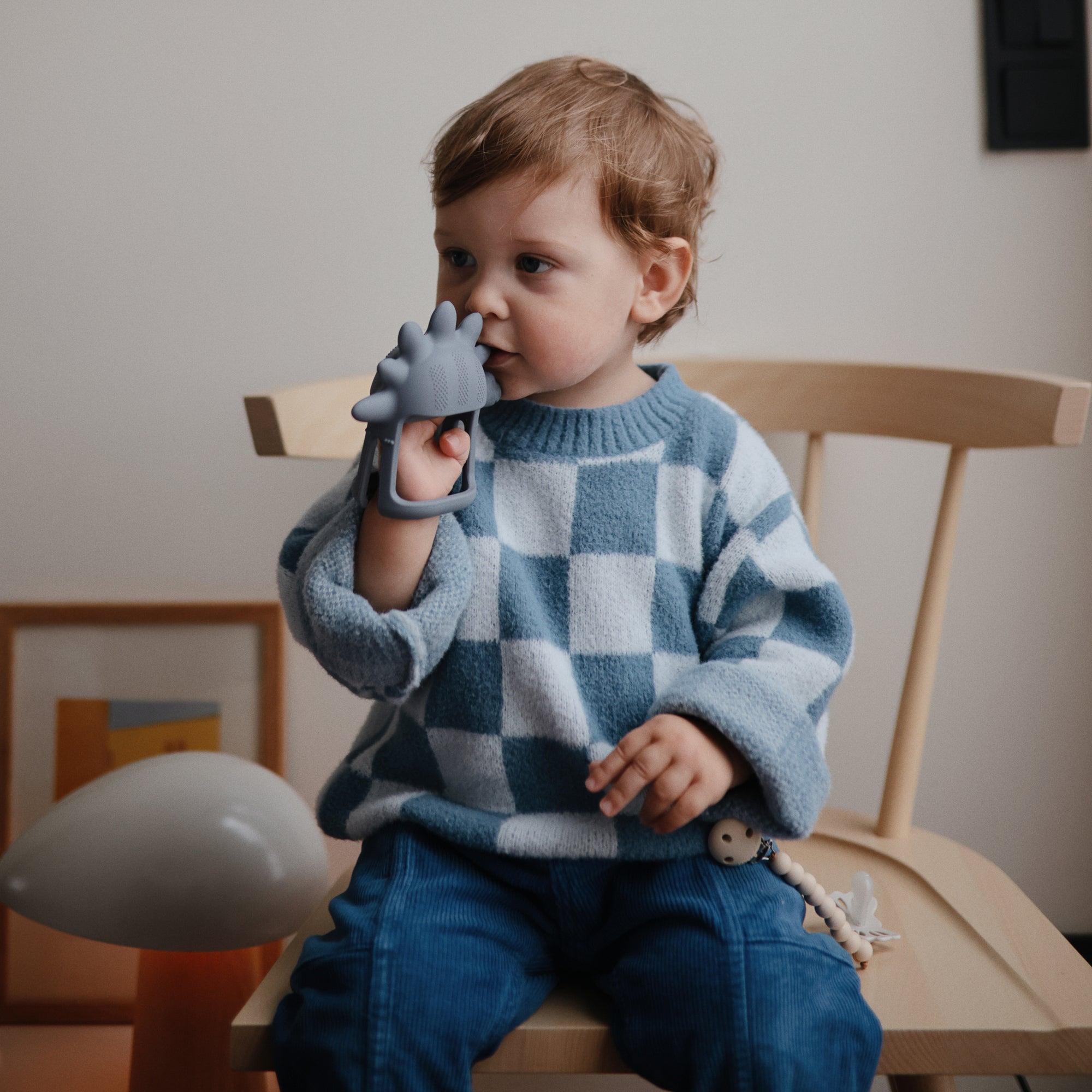 Toddler bites a mushie No-Drop Teether shaped like a dinosaur.