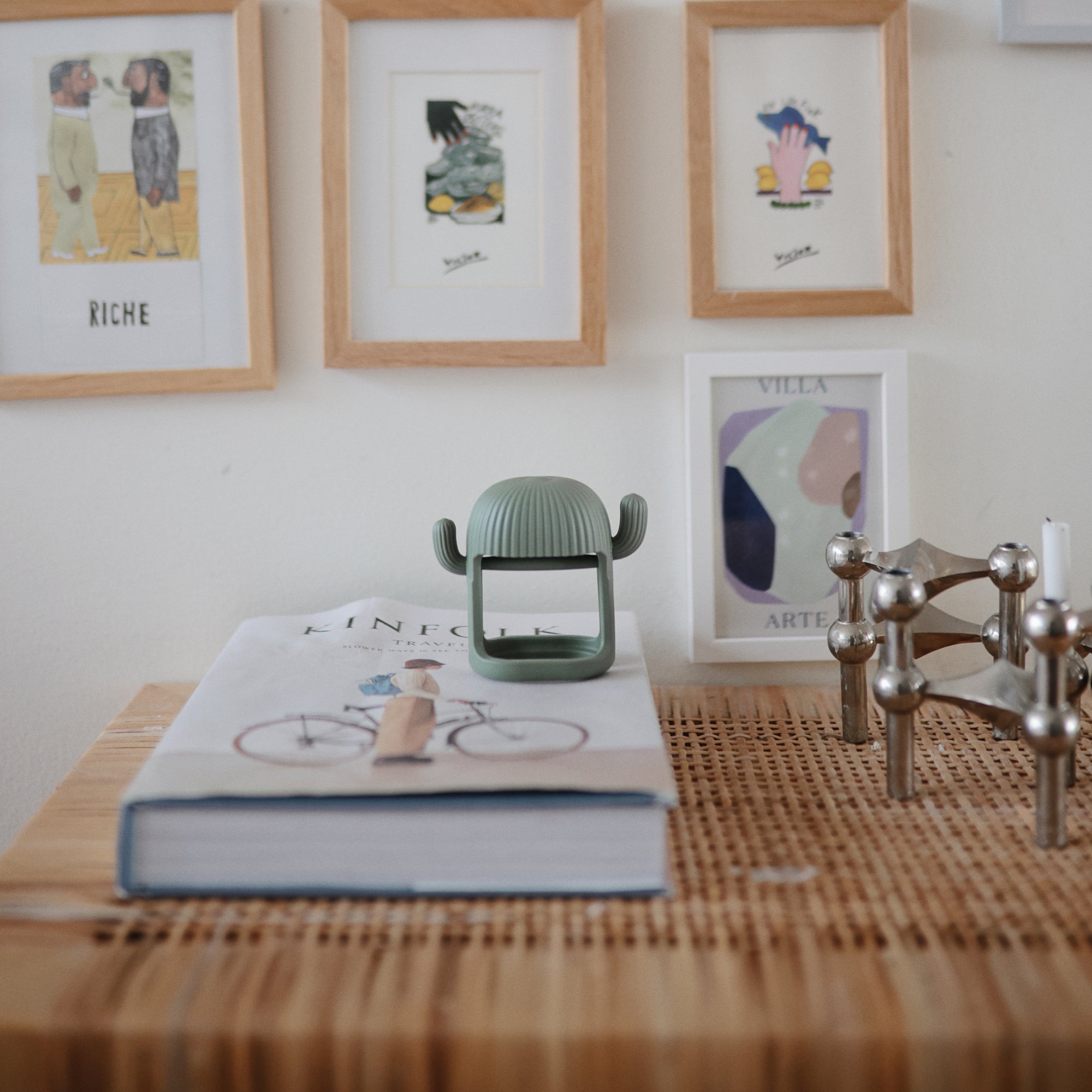 A book and decor on a table with a mushie No-Drop Teether and framed art in the background.