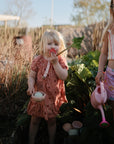 Two kids in a garden: one with a pink watering can, one with mushie's Nesting Spheres Sensory Toy.
