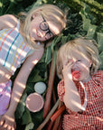 Two kids enjoy the mushie Nesting Spheres Sensory Toy, smiling while sitting on green leaves.