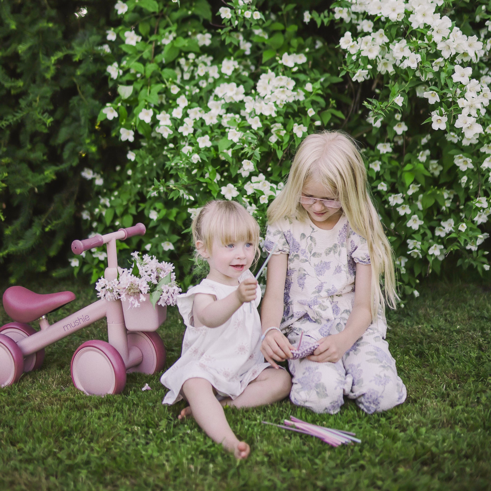 Two young girls on grass play with a mushie Silicone Sensory Toy, colored pencils nearby.