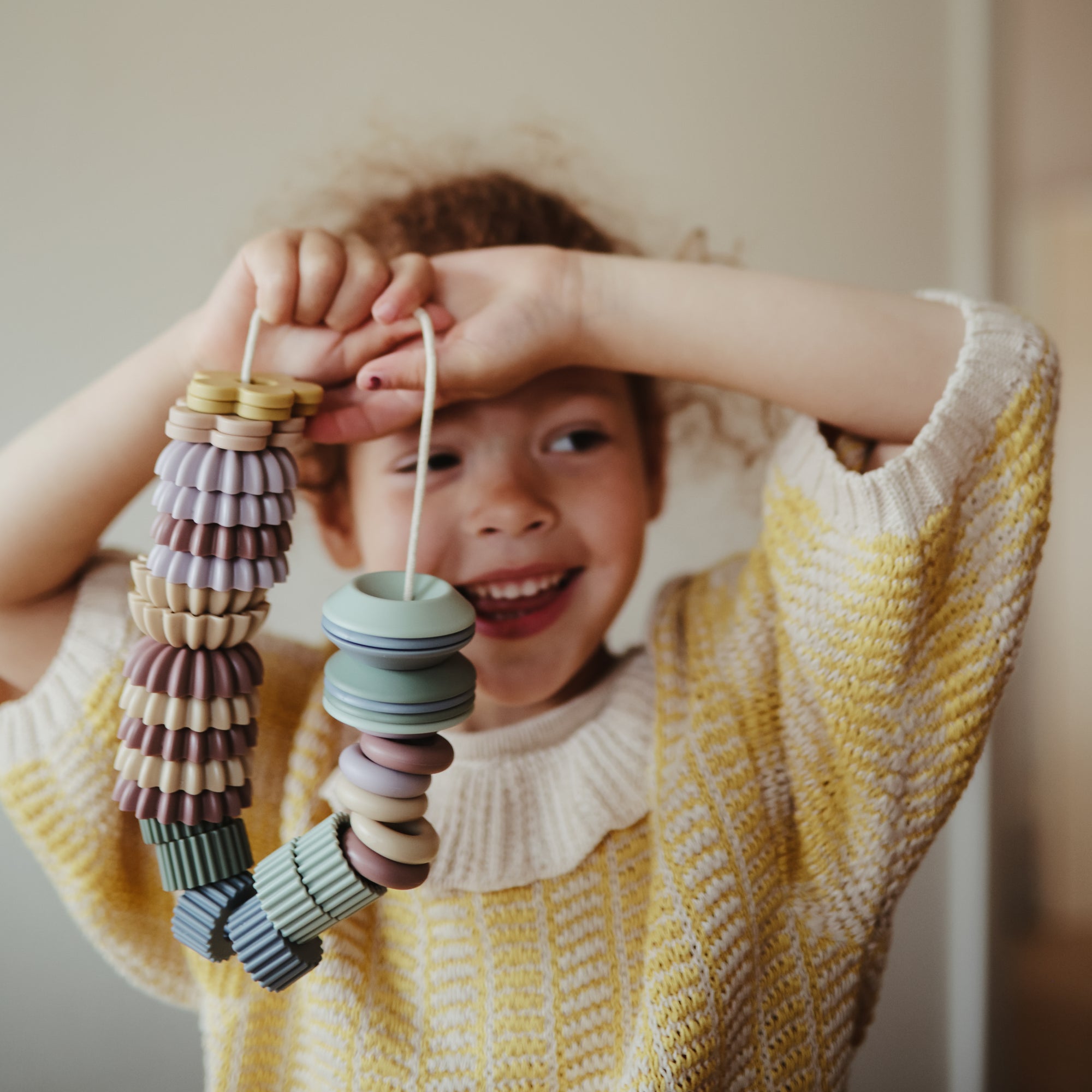 Smiling child with mushie Bead Lacing Toy Set, stacking rings for motor skill development.