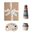 The mushie Playtime Gift Set ($48 value) comes neatly wrapped with a white ribbon and includes pastel sensory toys—a stacking toy, nesting cups, and a paint palette-shaped toy—to help develop fine motor skills. Shown on a white background.