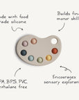 The mushie Paint Palette Press Toy features a beige base with seven colorful silicone circles. Made from food-grade silicone, it encourages sensory exploration, builds fine motor skills, and is free from BPA, BPS, PVC, and phthalates.