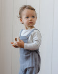 Toddler in blue overalls and Rylee + Cru Long Sleeve Tee Cloud Stripe by a white paneled wall.