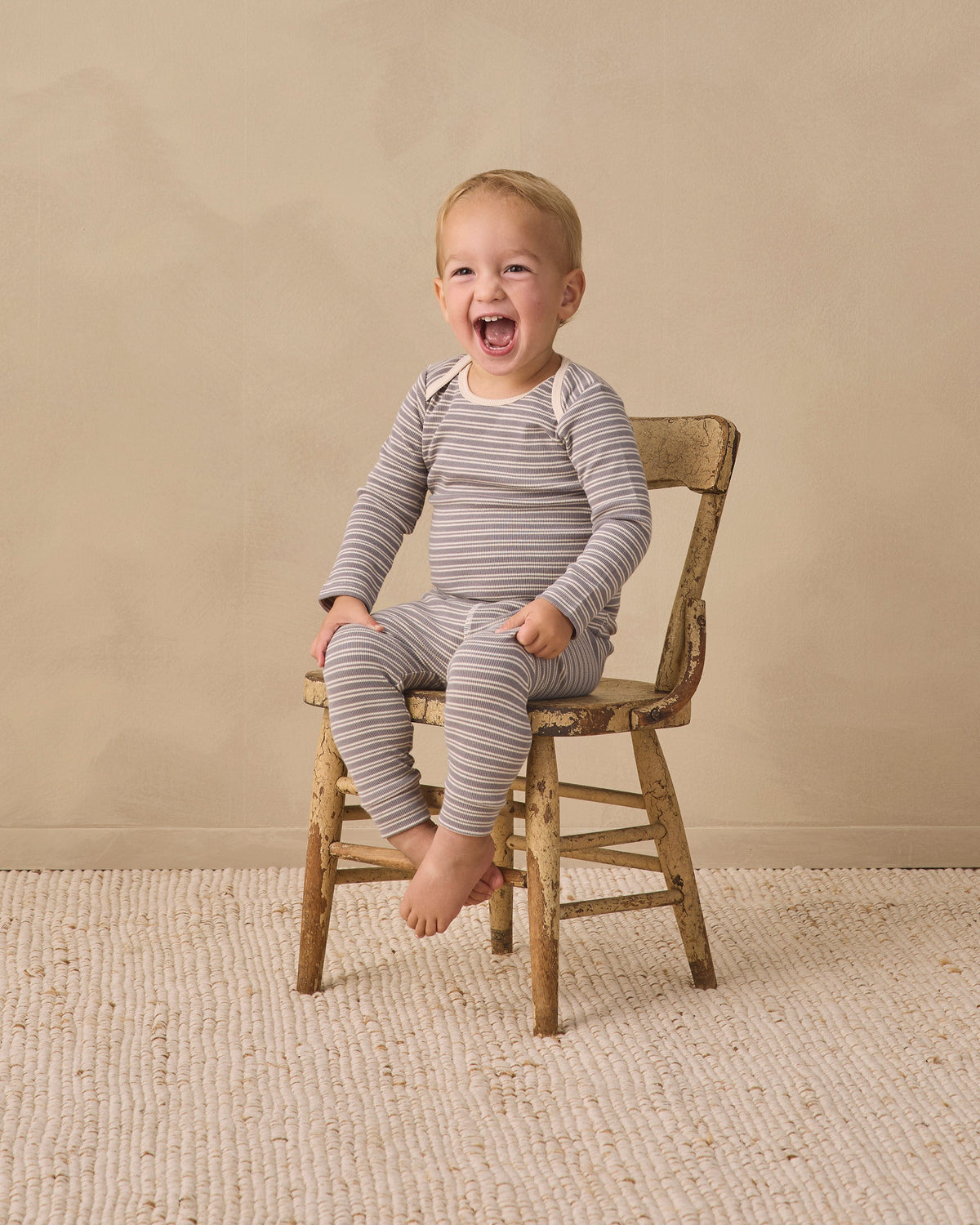 Smiling toddler in Rylee + Cru Ribbed Tee + Legging Set Slate Microstripe on wood chair.