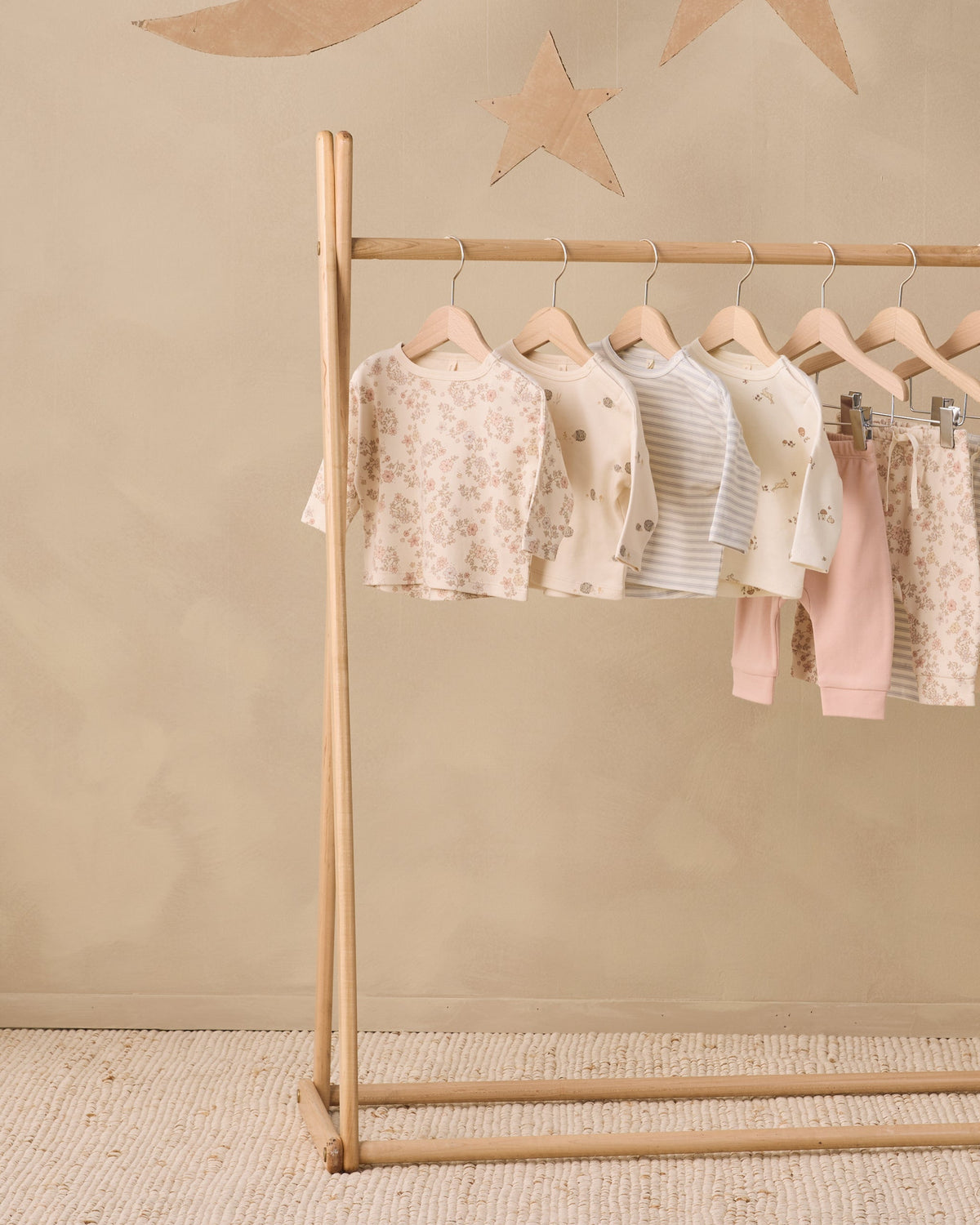 Six Rylee + Cru Cloud Stripe tees hang on a rack against a beige wall with star decorations.