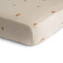 A close-up of the mushie Stretchy MINI Crib Sheet in light beige, adorned with small brown minimalist rainbows. Made from breathable organic cotton, the sheet fits snugly around a mini crib mattress corner.