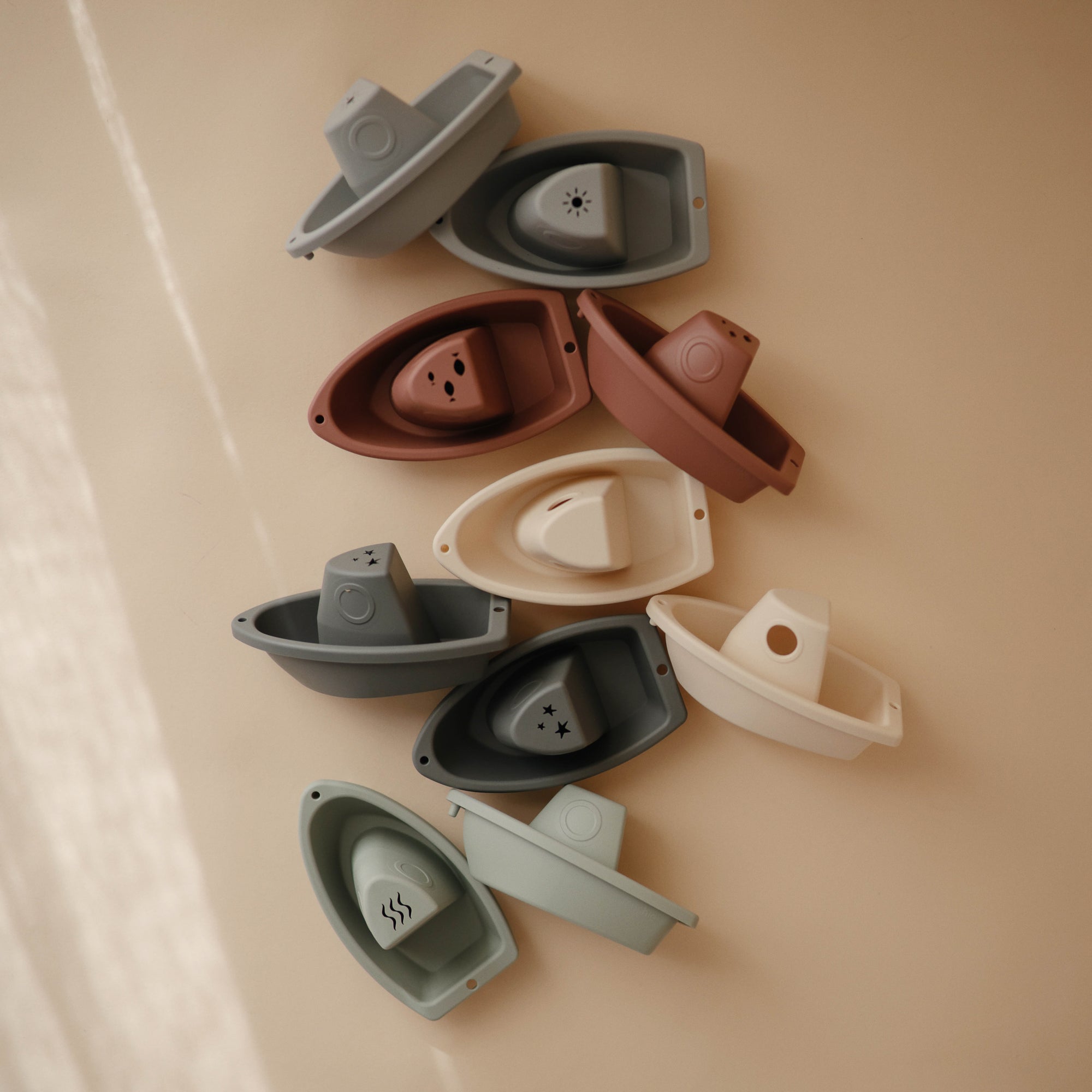 Mushie Bath Boats in muted colors—stackable water play toys on a beige surface.