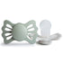 The FRIGG Lucky Symmetrical Silicone Pacifier 2-Pack (6-18 Months) in Sage/Silver Gray features butterfly-shaped shields and medical-grade silicone nipples—designed by FRIGG to support healthy oral development.