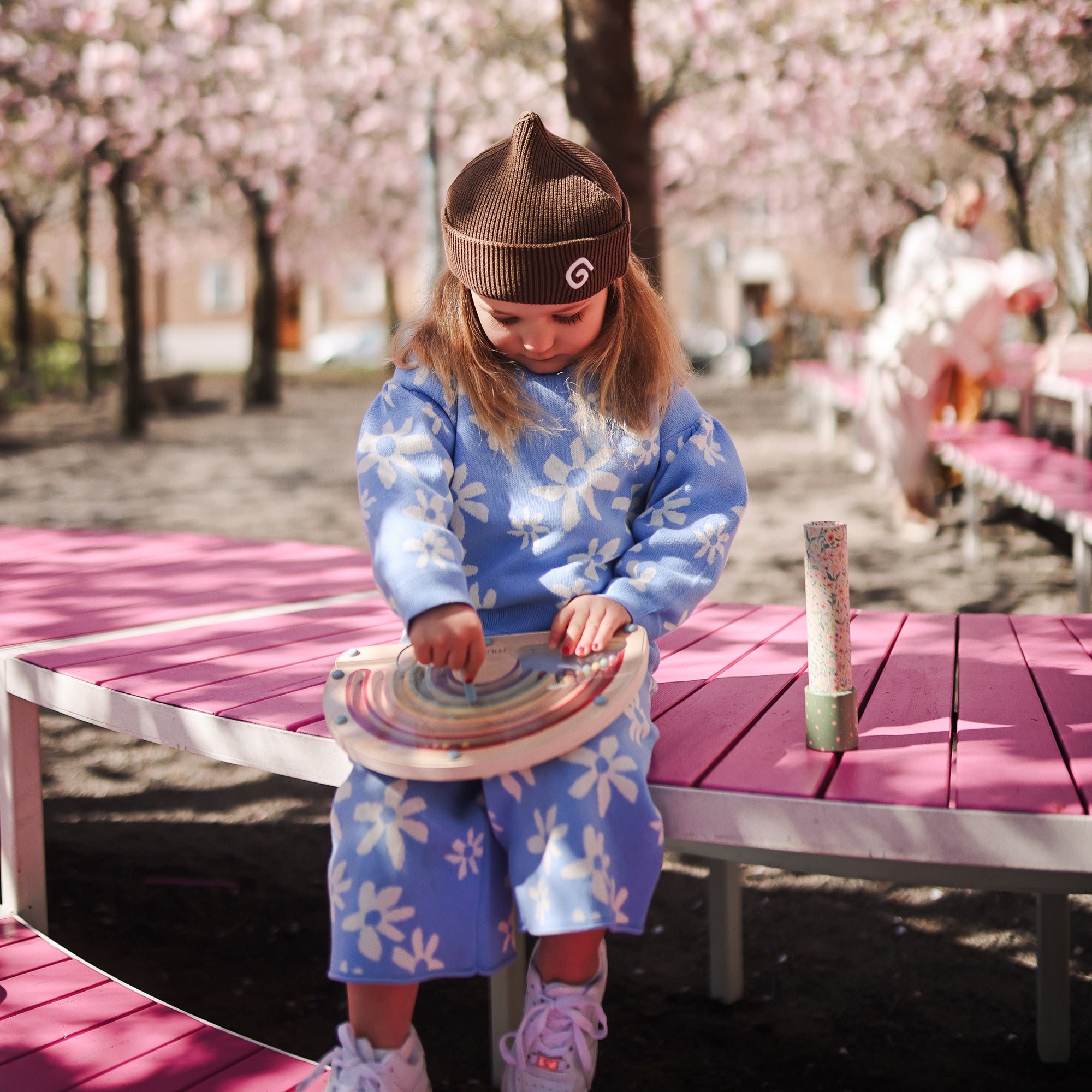 A young girl plays with the mushie Wooden Magnetic Rainbow Maze on a pink bench.