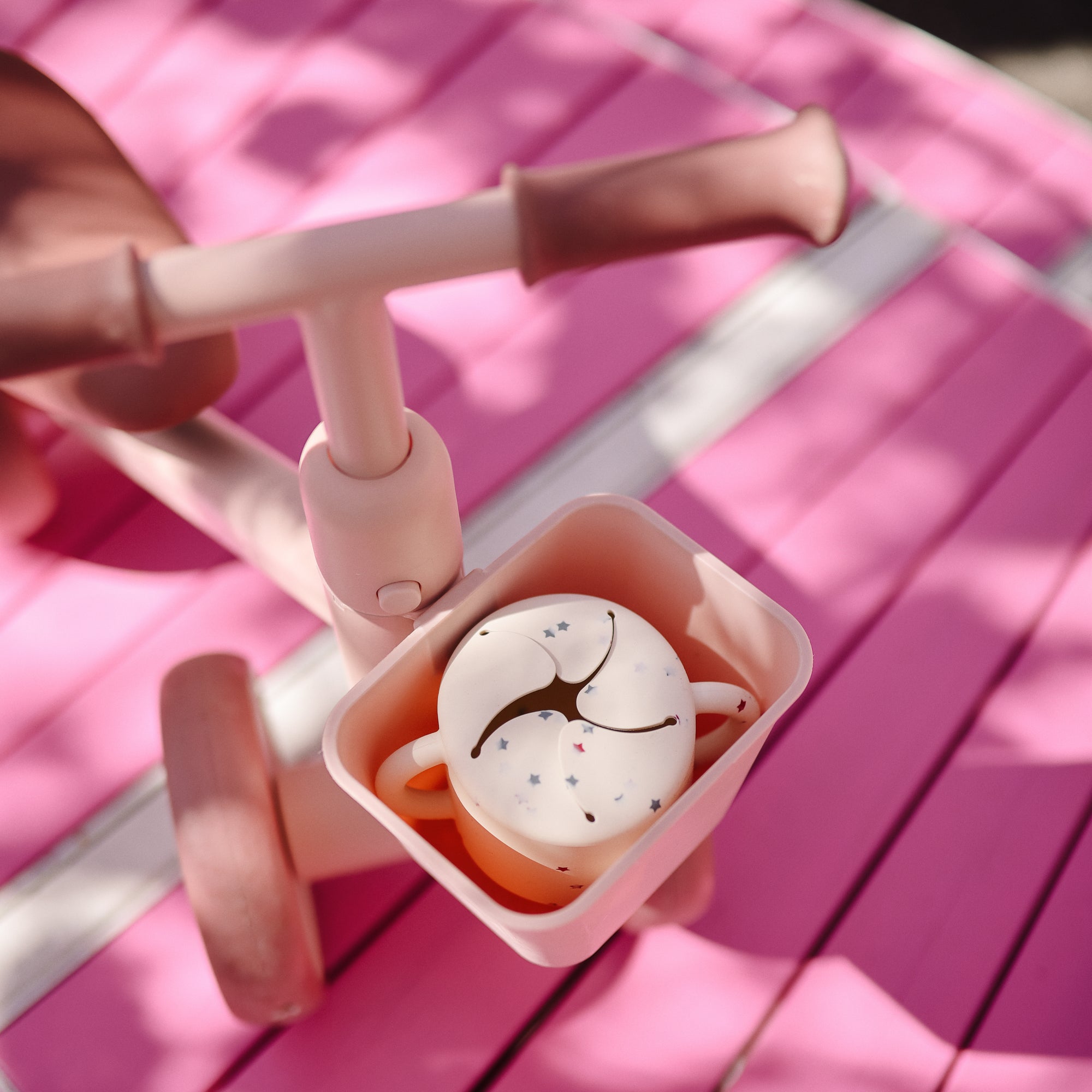 Pink toddler tricycle with a mushie Snack Cup, spill-proof and silicone, in the basket.