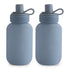 Two grayish-blue Silicone Puree Pouches from mushie, featuring rounded edges, screw-on lids, and looped handles, stand side by side on a white background. The "mushie" logo is embossed on each for mess-free feeding on the go.