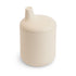 The Mushie Silicone Sippy Cup is beige, cylindrical with a rounded lid and small spout, crafted for young children’s feeding needs.