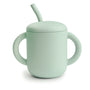 The Mushie Silicone Training Cup + Straw is a light green baby cup with two large handles and a matching lid with an angled straw, perfect for little ones learning to drink independently.