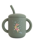 Mushie Silicone Training Cup + Straw, green with handles and skating bunny on front.